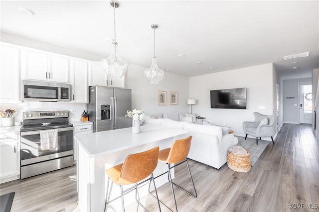 kitchen with open floor plan, stainless steel appliances, light countertops, and white cabinets