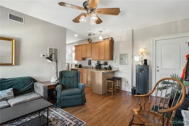 living area featuring wood-type flooring, visible vents, a ceiling fan, electric panel, and baseboards