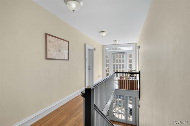 corridor featuring wood finished floors, an upstairs landing, and baseboards