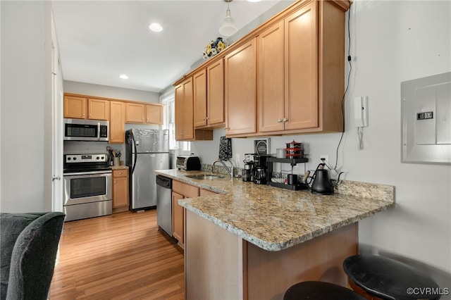 kitchen featuring electric panel, a peninsula, stainless steel appliances, light wood-style floors, and a sink