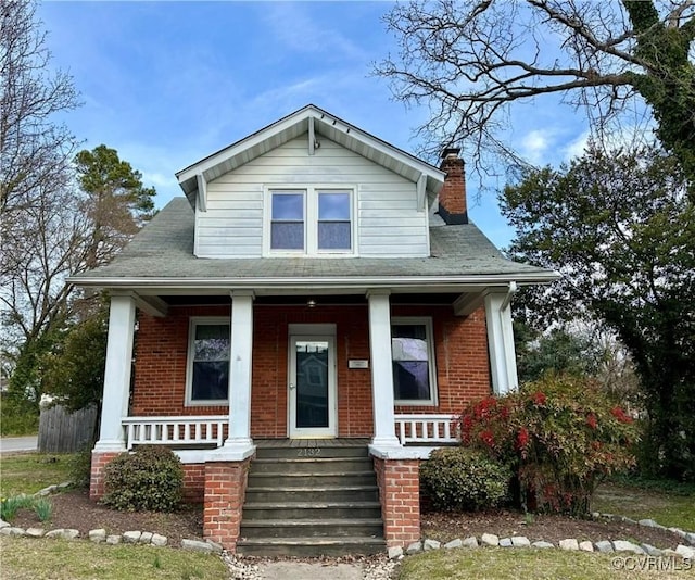 bungalow with a chimney, a porch, and brick siding