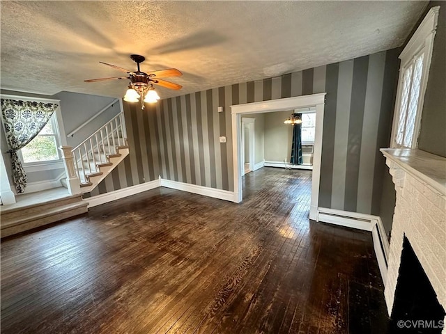 unfurnished living room with a textured ceiling, baseboards, stairway, hardwood / wood-style floors, and wallpapered walls