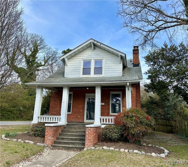 view of front of house with a porch, brick siding, fence, and a chimney