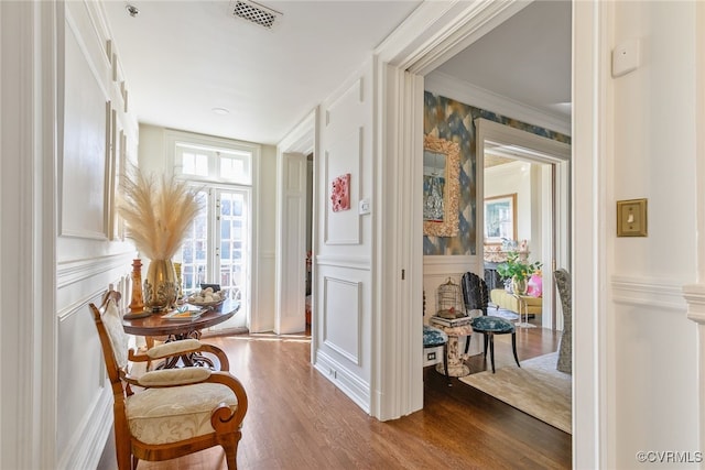 living area featuring visible vents, dark wood finished floors, wainscoting, ornamental molding, and a decorative wall