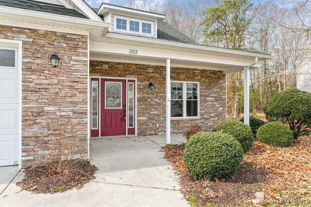 doorway to property featuring a garage, stone siding, covered porch, and a shingled roof