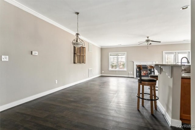 kitchen featuring a warm lit fireplace, visible vents, ornamental molding, dark wood-style floors, and a kitchen bar