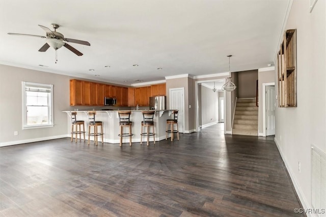 kitchen featuring dark wood-type flooring, a breakfast bar, appliances with stainless steel finishes, brown cabinetry, and crown molding