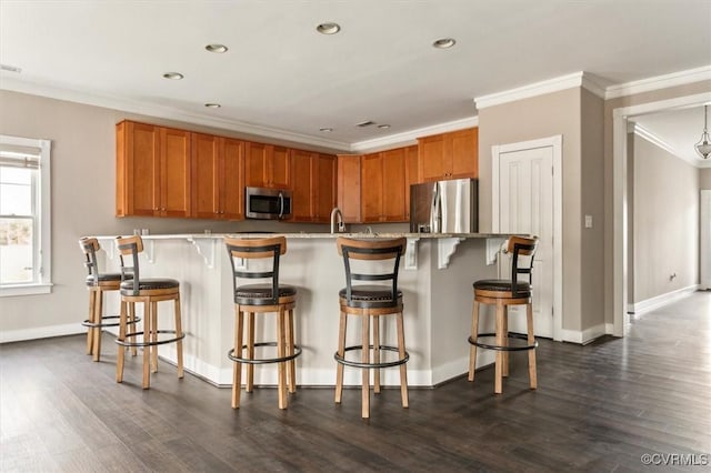 kitchen with appliances with stainless steel finishes, a breakfast bar, dark wood-style flooring, ornamental molding, and light countertops