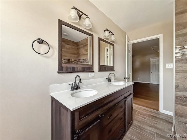 full bathroom featuring double vanity, wood finished floors, a sink, and baseboards