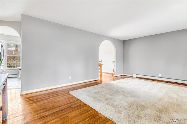 unfurnished room featuring baseboards, a baseboard radiator, arched walkways, and light wood-style floors