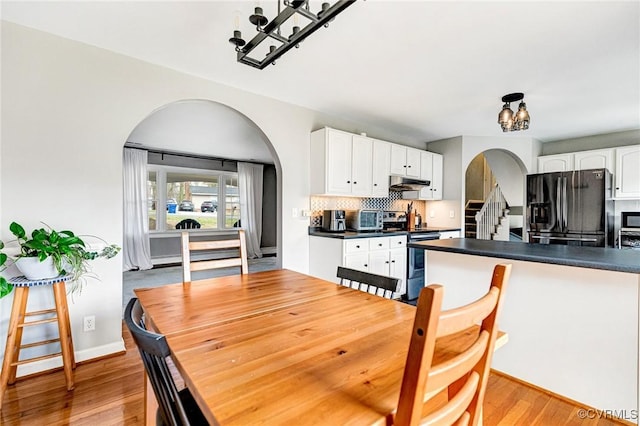 dining area with arched walkways, stairway, and light wood finished floors