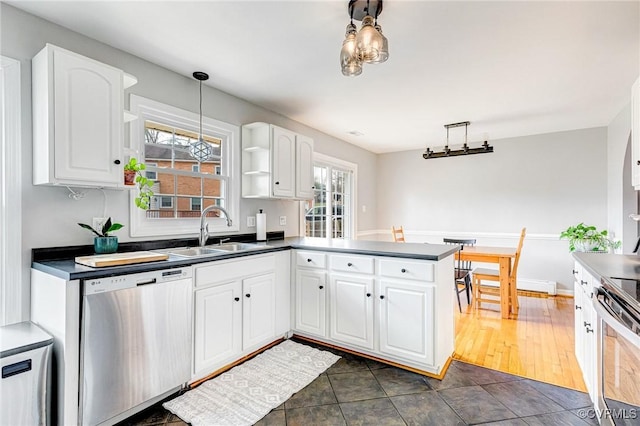 kitchen with white cabinets, dark countertops, appliances with stainless steel finishes, a peninsula, and a sink