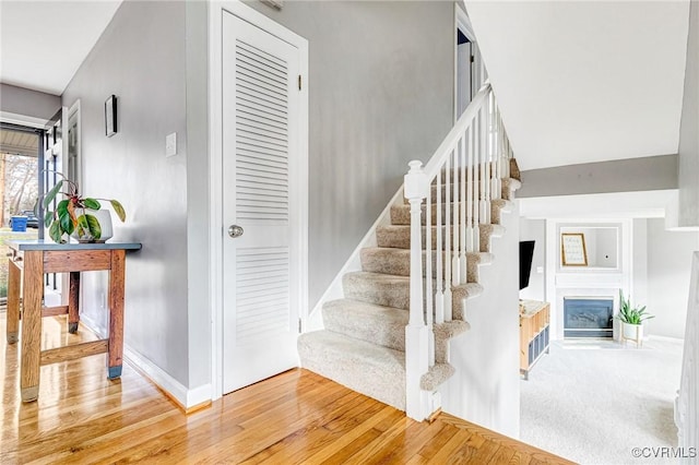 stairs with a fireplace with flush hearth, carpet floors, baseboards, and wood finished floors