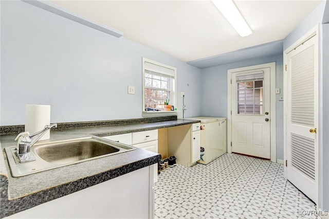 kitchen featuring a sink, white cabinets, light floors, built in desk, and dark countertops