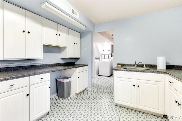 kitchen with separate washer and dryer, dark countertops, a sink, and white cabinets