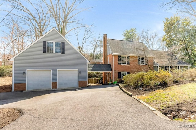 view of front of property with brick siding, a chimney, a shingled roof, and aphalt driveway