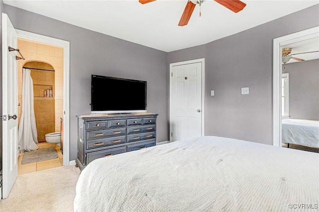 bedroom featuring light colored carpet, ceiling fan, and ensuite bath