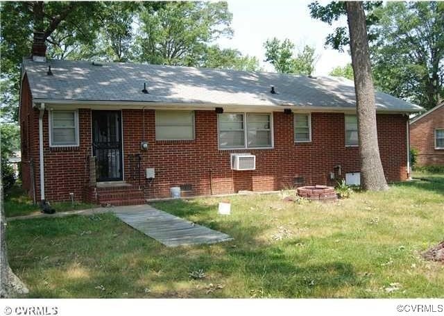 view of front of house with brick siding, an AC wall unit, an outdoor fire pit, and a front yard