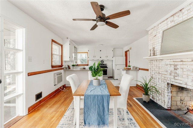 dining space featuring ceiling fan, light wood-style flooring, a fireplace, visible vents, and baseboards