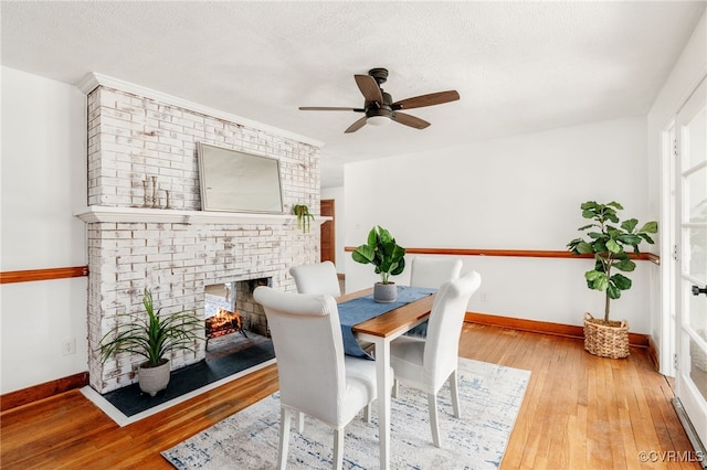 dining space featuring a textured ceiling, a fireplace, hardwood / wood-style flooring, and baseboards