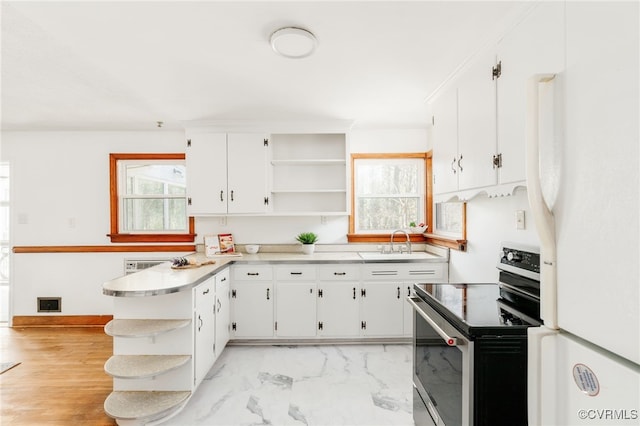 kitchen with white cabinets, stainless steel electric range oven, freestanding refrigerator, open shelves, and a sink