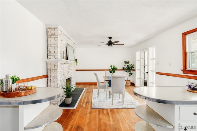 living area with light wood-style flooring, a brick fireplace, ceiling fan, a textured ceiling, and baseboards