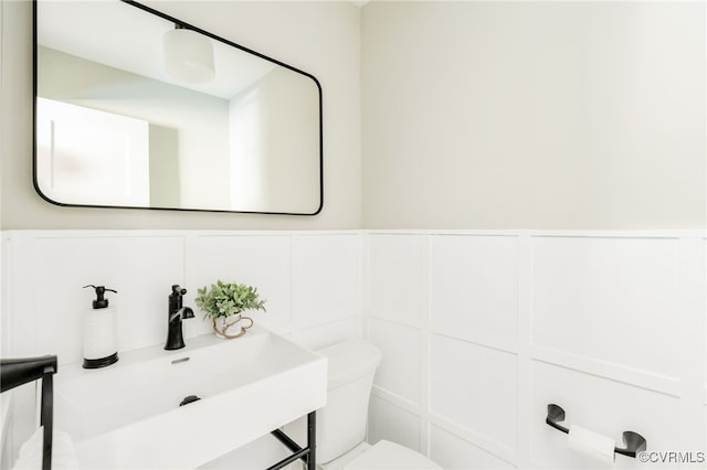 half bath featuring wainscoting, a sink, toilet, and a decorative wall