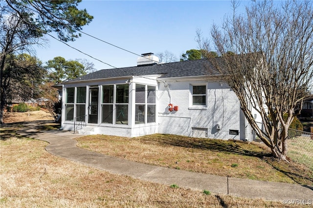 back of house with brick siding, fence, a sunroom, a lawn, and a chimney