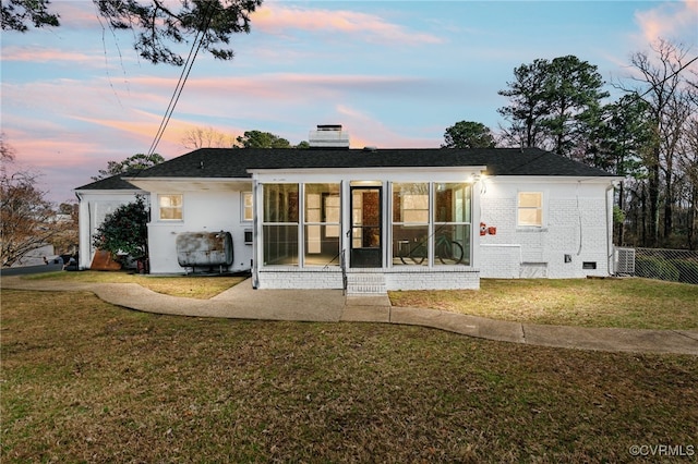 back of property at dusk with a sunroom, a chimney, crawl space, a yard, and brick siding