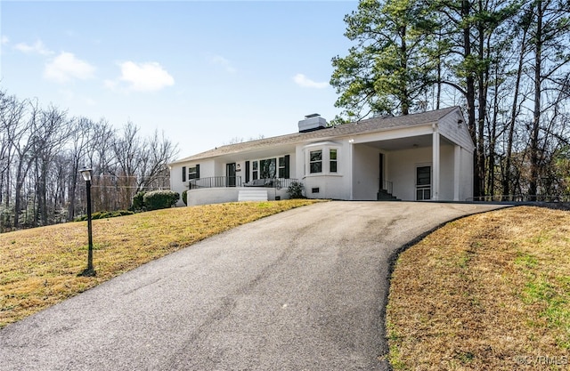 ranch-style home with driveway, stucco siding, a carport, a chimney, and a front yard