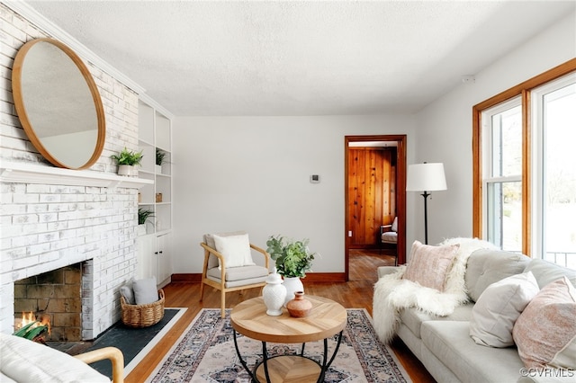 living room with a brick fireplace, a textured ceiling, baseboards, and wood finished floors