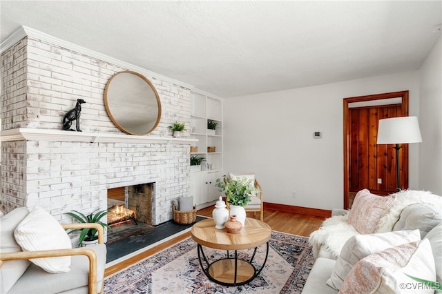 living area featuring a textured ceiling, a fireplace, wood finished floors, and baseboards