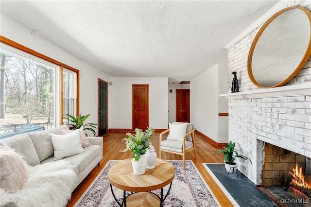 living area with a textured ceiling, a fireplace, wood finished floors, and baseboards