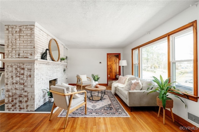 living room with a textured ceiling, a brick fireplace, and wood finished floors