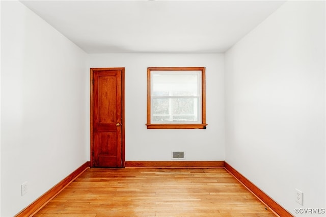 empty room with light wood finished floors, visible vents, and baseboards