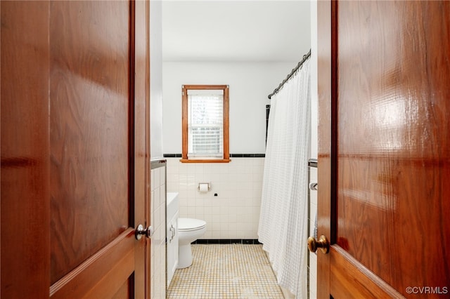 full bath featuring toilet, a wainscoted wall, tile patterned flooring, and tile walls