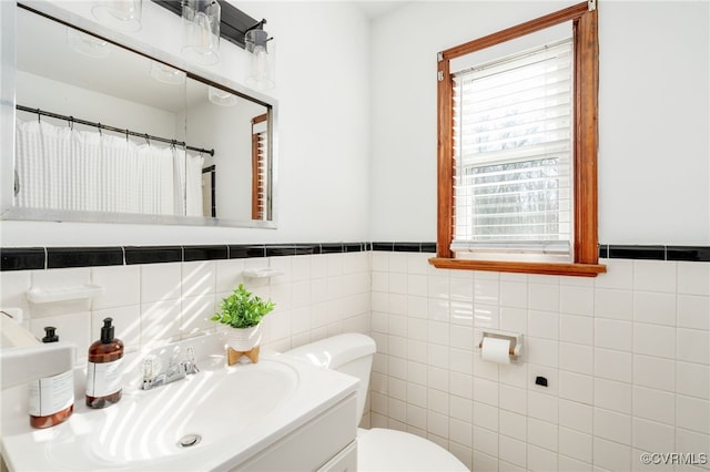 bathroom featuring a wainscoted wall, tile walls, a shower with shower curtain, toilet, and a sink