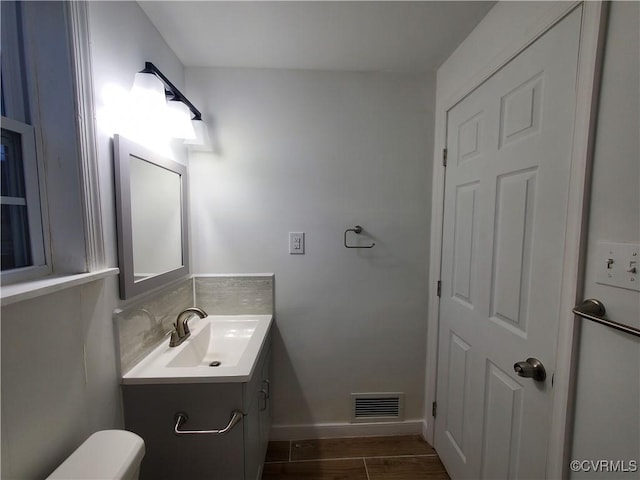 half bath featuring baseboards, visible vents, toilet, wood finished floors, and vanity