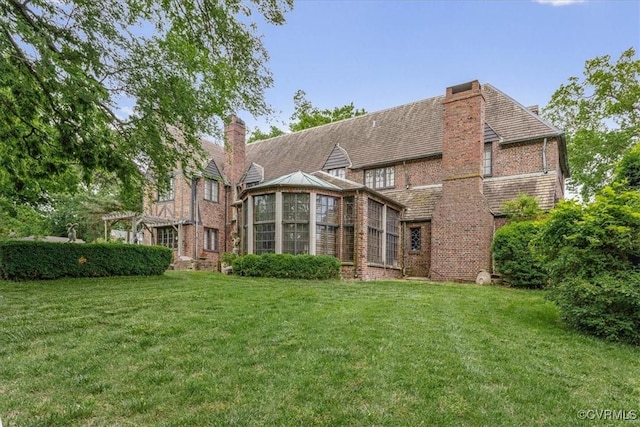 rear view of property with brick siding, a lawn, and a chimney