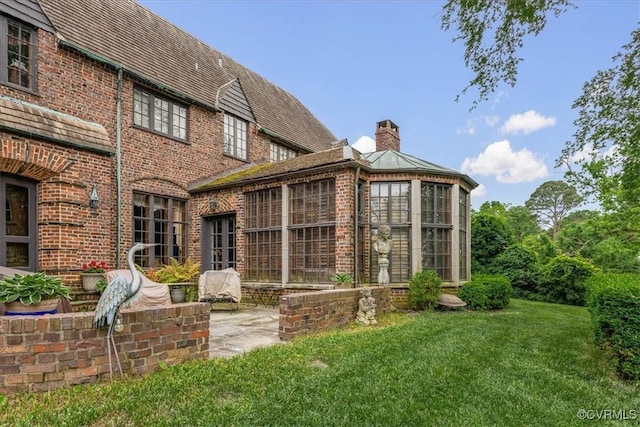 exterior space featuring a chimney, a yard, brick siding, a patio, and a sunroom