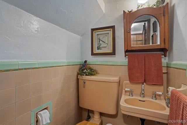 bathroom with tile walls, a wainscoted wall, a sink, and toilet