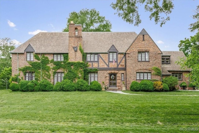 tudor house with brick siding, a chimney, and a front yard