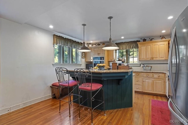 kitchen with freestanding refrigerator, light wood-style flooring, a kitchen bar, and light brown cabinetry