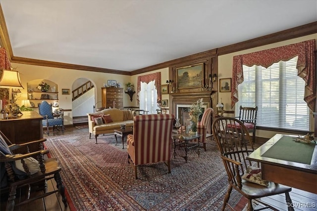 living area featuring baseboards, arched walkways, ornamental molding, wood finished floors, and a fireplace