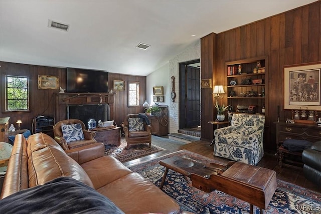 living area with visible vents, a fireplace, vaulted ceiling, and wood walls