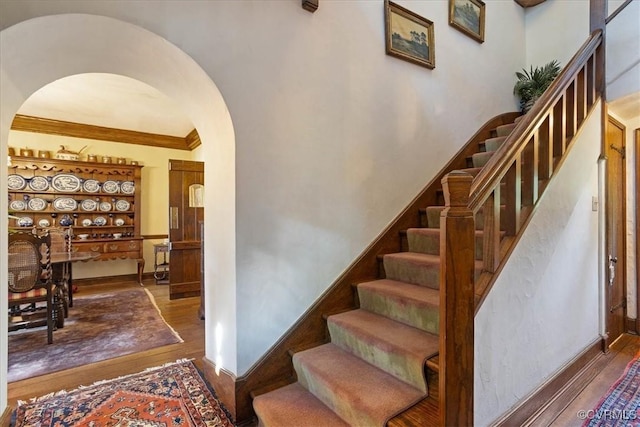 stairway with arched walkways, wood finished floors, and crown molding