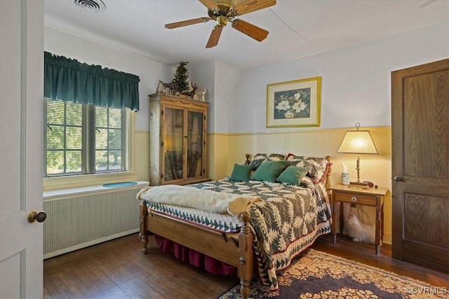 bedroom with a ceiling fan, a wainscoted wall, radiator, wood-type flooring, and visible vents