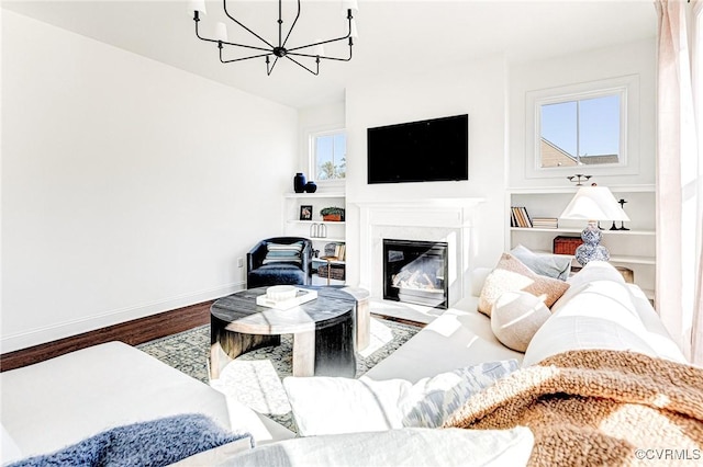 living room with baseboards, a chandelier, wood finished floors, and a glass covered fireplace