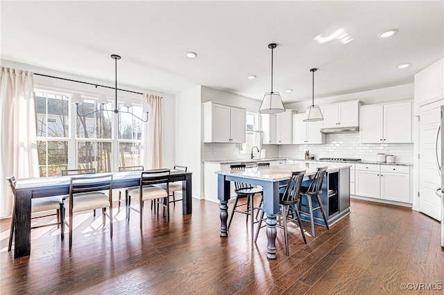 kitchen featuring under cabinet range hood, a kitchen island, a kitchen breakfast bar, tasteful backsplash, and dark wood finished floors