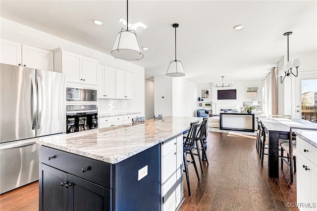 kitchen with black oven, white cabinetry, dark wood-type flooring, and freestanding refrigerator